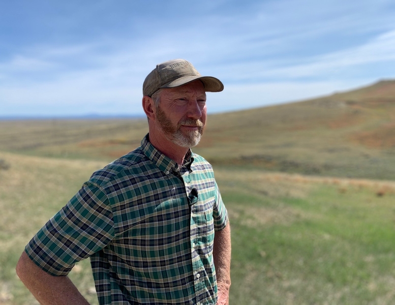 A farmer wearing a baseball cap stands in a field.
