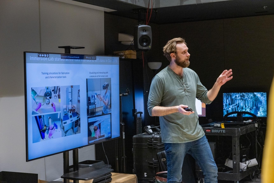 Talis Reks stands in front of a large monitor, speaking to an unseen audience