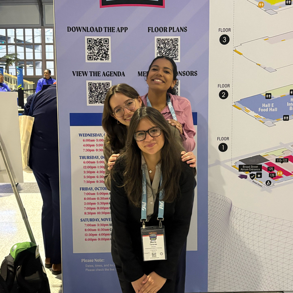 Isabel Duran and two friends crouch in front of a map at a convention center. They wear attendee badges.