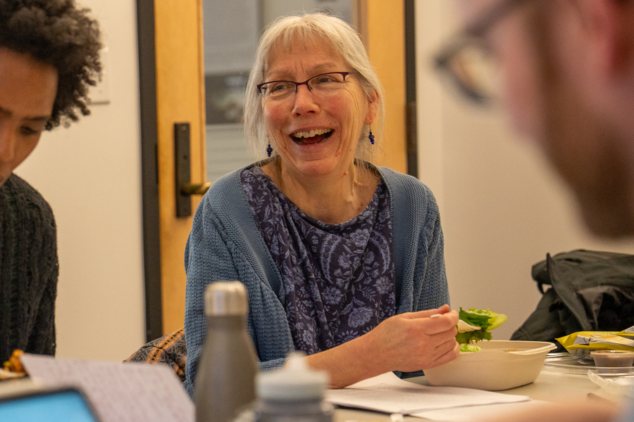Anne McCants, seated at a table and eating a salad, laughs