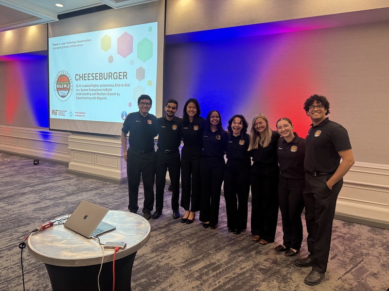 8 individuals dressed identically in black stand next to their powerpoint presentation.