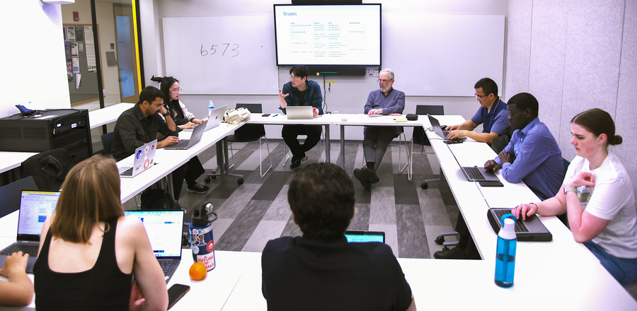 10 people sit at a square table in a small classroom