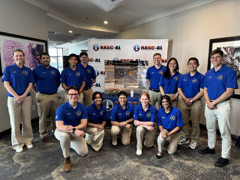 13 individuals wearing blue uniforms pose together in front of a RASC-AL banner.