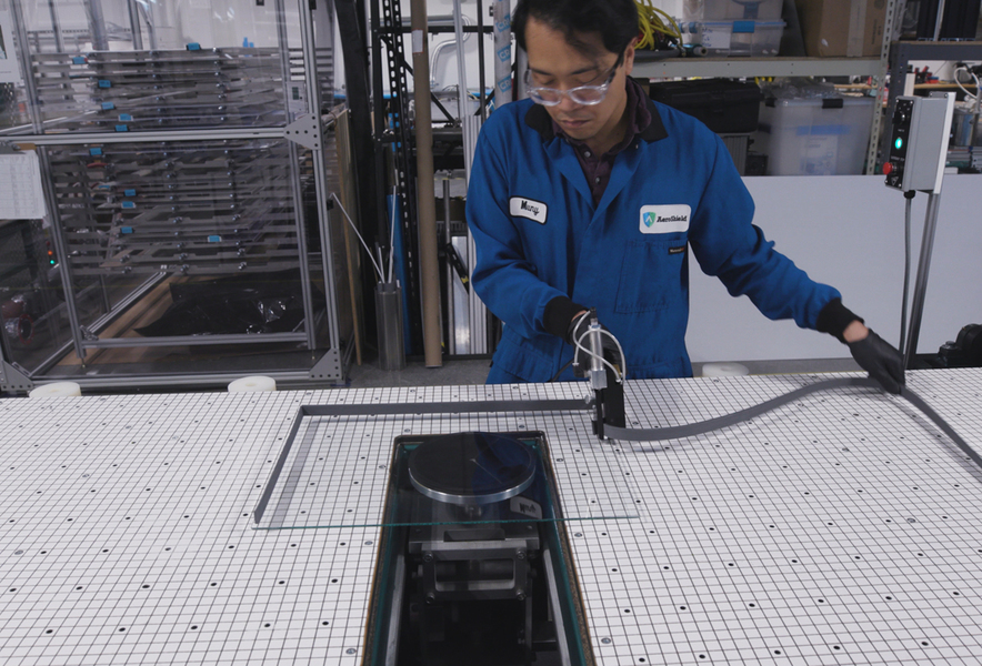 A person in a blue jumpsuit operates a power tool on a large table marked with grid lines
