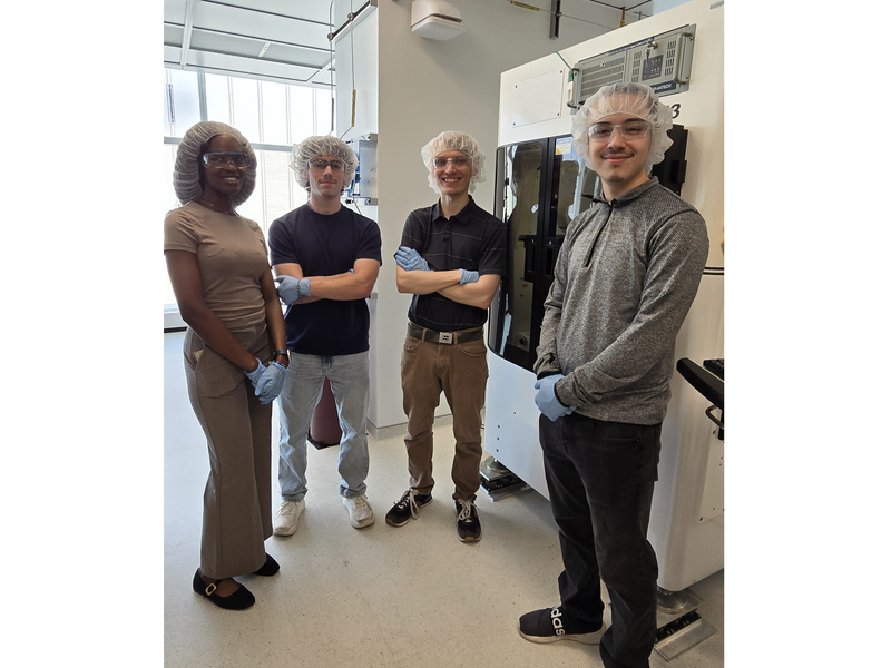 Four people wearing hairnets and nitrile gloves stand in a lab.