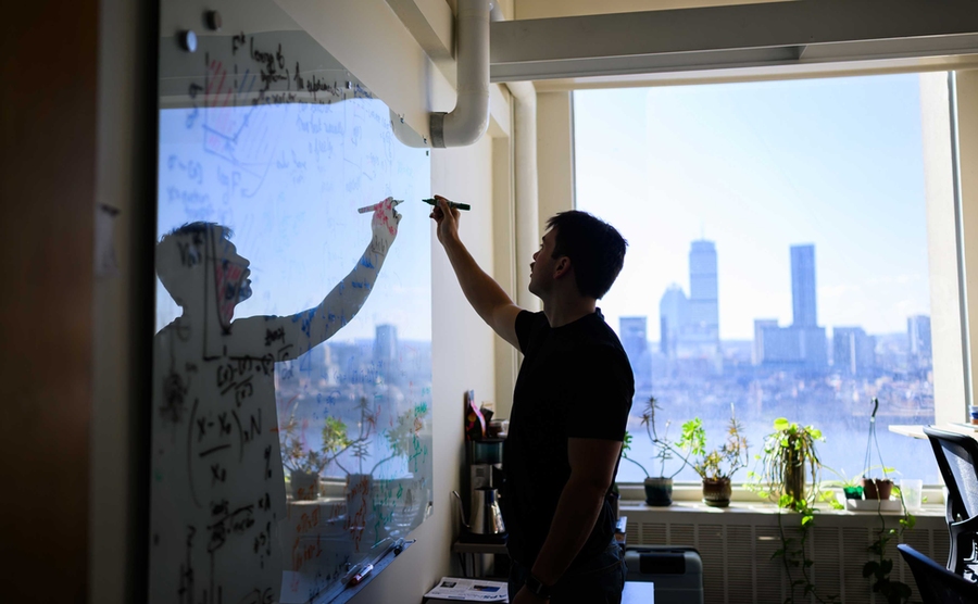 Perrin Davidson, seen in silhouette writing on a whiteboard, with the Charles River and Boston in the background