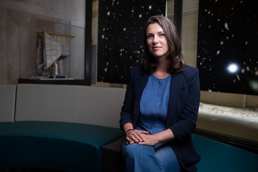 Erin Kara seated with large posters of galaxies in background.