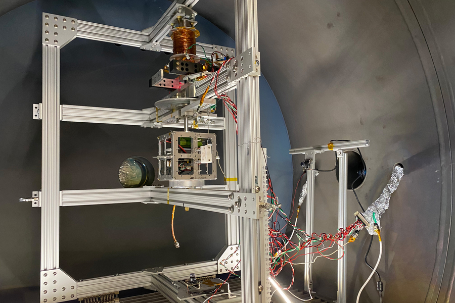 Photo of the "MagLev" thrust stand, which contains several interconnected metal brackets supporting wires and electrical equipment inside a large cyllindrical container