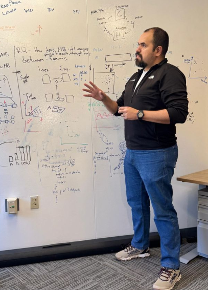 Ignacio Vazquez gestures in front of whiteboard covered with symbols and diagrams