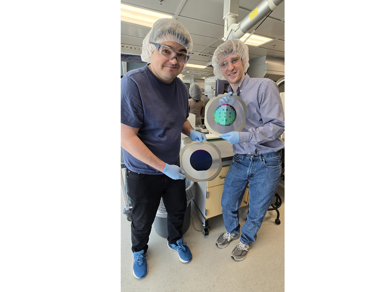 Two men wearing hairnets pose with a wafer the size of a dinner plate.