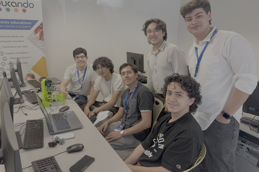 Four students seated at a table and two standing behind them smile at the camera