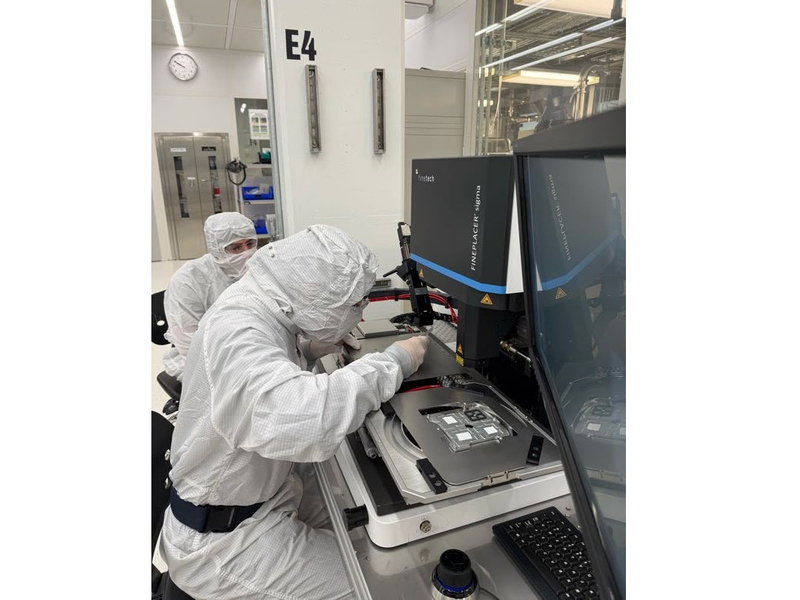 Two people in bunny suits sit before a complex piece of machinery in MIT.nano's cleanroom.