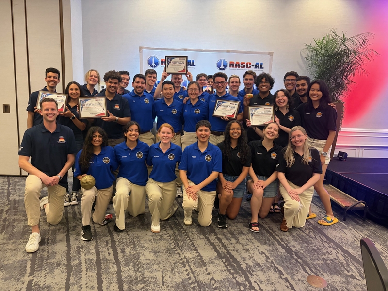 A group photo of about 30 RASC-AL winners, all wearing their team uniforms, with four students holding their award certificates. Everyone is smiling and some hold up other props.