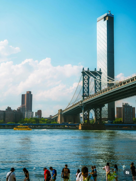 The Brooklyn Bridge is framed by clouds and water on a bright summer day. 