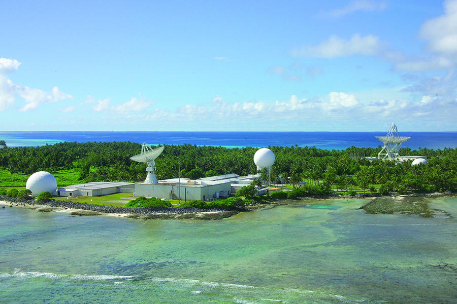Two radar domes and two radar dishes sit on a tropical island on a sunny day