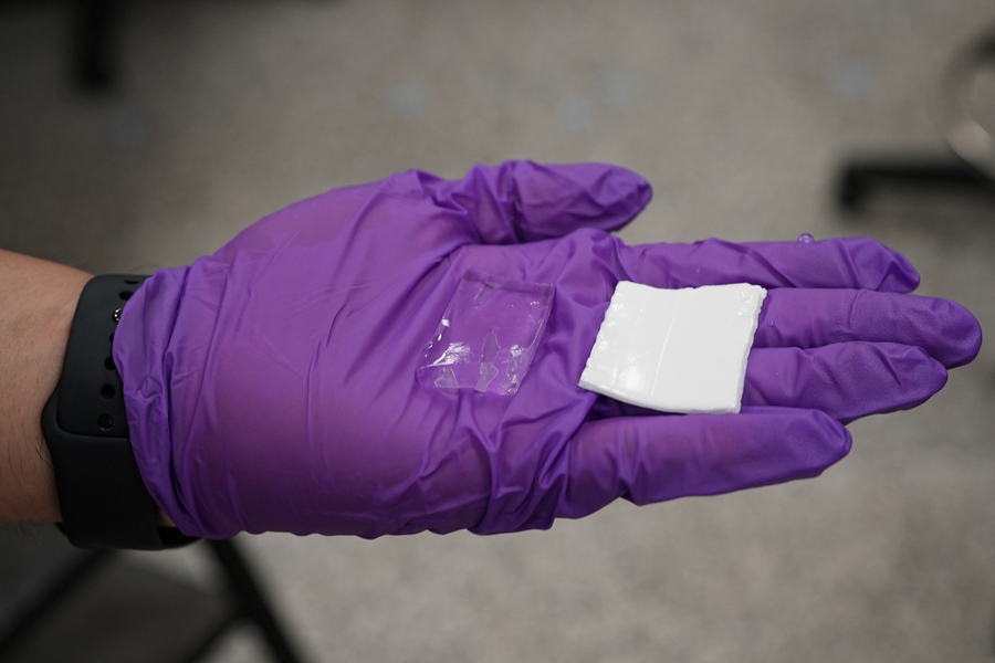 A gloved hand holds two square examples of hydrogel, one clear and one white.