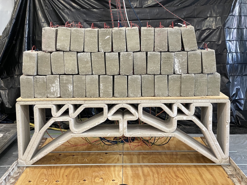 Printed concrete bridge the size of a park bench holds 3 layers of concrete blocks on top