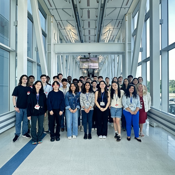 Group of about 30 students standing together in a daylit hallway 