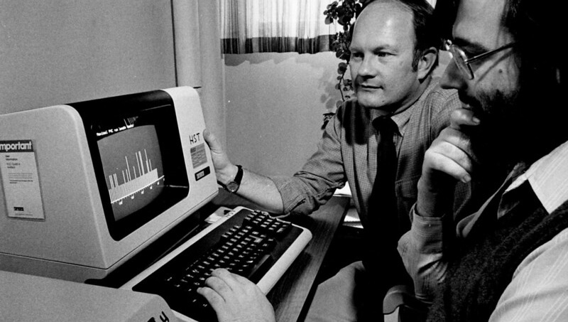 Grayscale photo of Roger Mark and George Moody looking at an early computer's small screen
