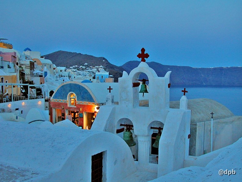 Whitewashed buildings, typical of the Greek islands, glow a soft blue in the light of dusk. In vivid contrast to its surroundings, one spotlit wall is painted bright orange