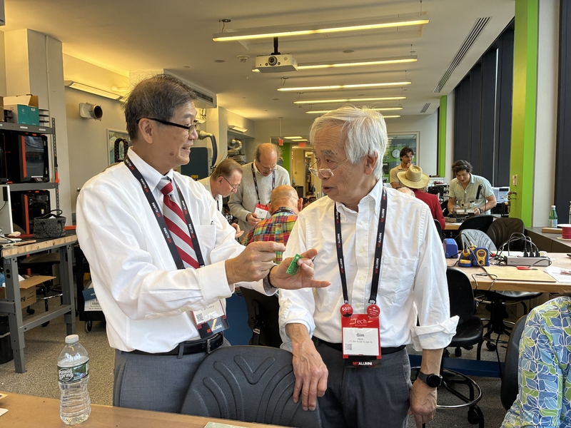 Gim Hom chats with one of his classmates at their 55th-year reunion over a working electronics bench. 