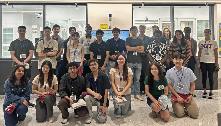 23 students wearing lanyards pose in a hallway with windows showing inside a clean lab