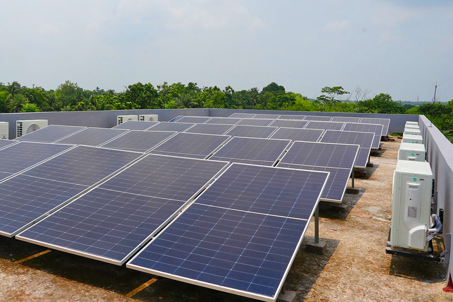 A flat roof in a wooded area covered in solar panels with heat pumps along the sides