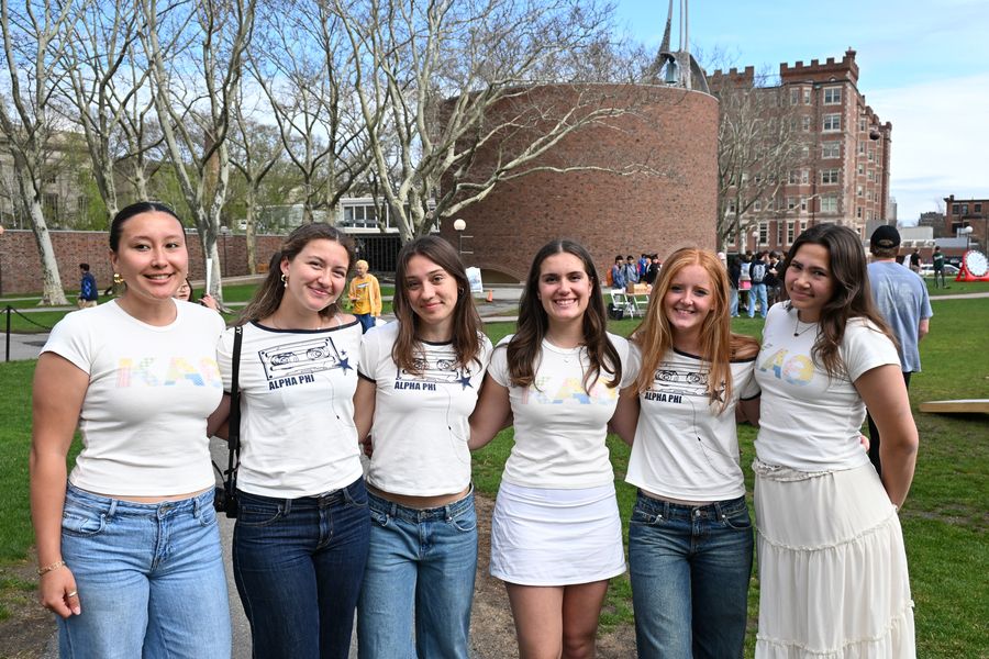 Six female students, all wearing white with "Alpha Phi" on their shirts, pose together on a courtyard in front of the MIT Chapel 