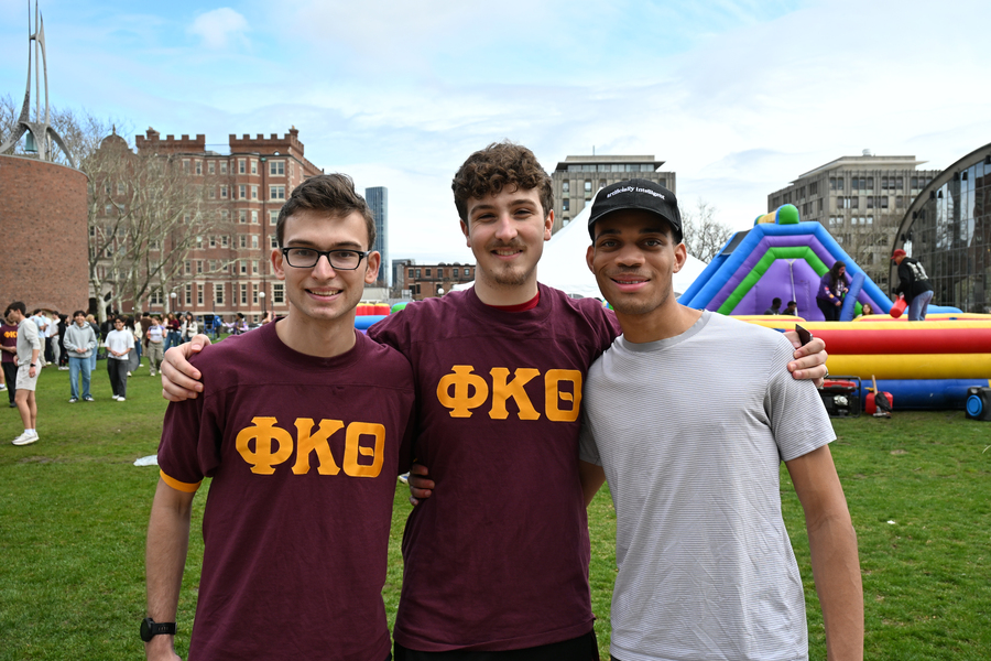 Three students, two of them wearing fraternity T-shirts, stand in front of a bouncy slide on the MIT campus