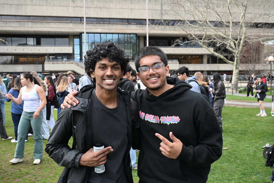 Two male students pose standing with their arms around one another in front of MIT's student center on a spring day