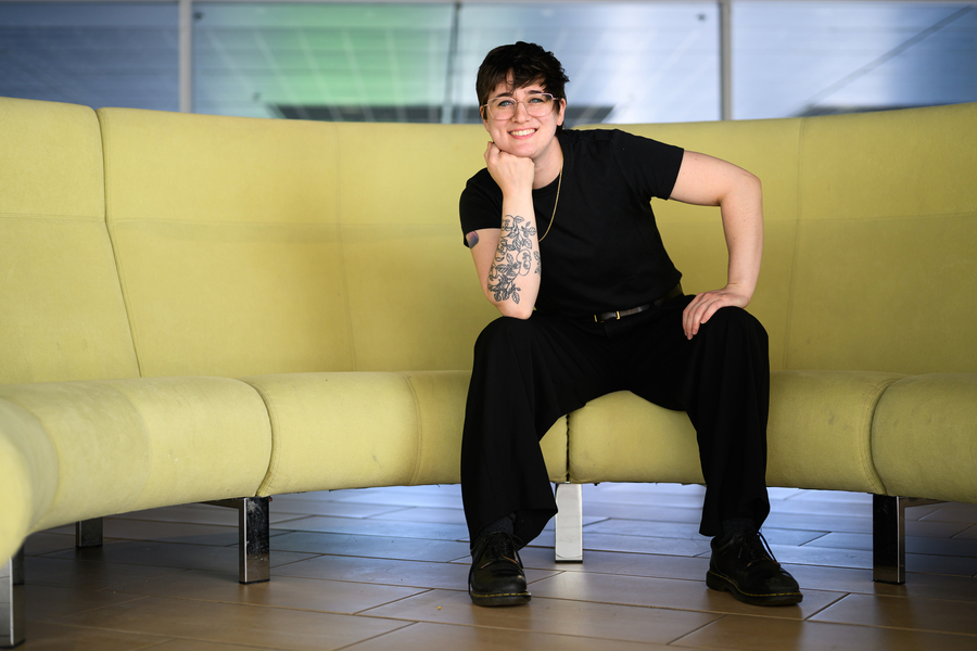 Shannon Knight portrait, seated on curved yellow couch. An intricate forearm tattoo with leaves and faces is visible.