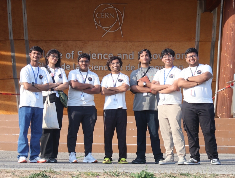 Manu Srivastava and 6 high school students pose standing in front of a sign at CERN with their arms folded
