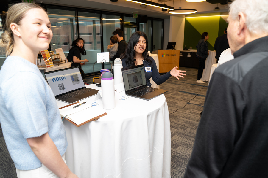Malia Smith and Shreya Agarwal present their project to a bystander. Their work is seen on two open laptops.
