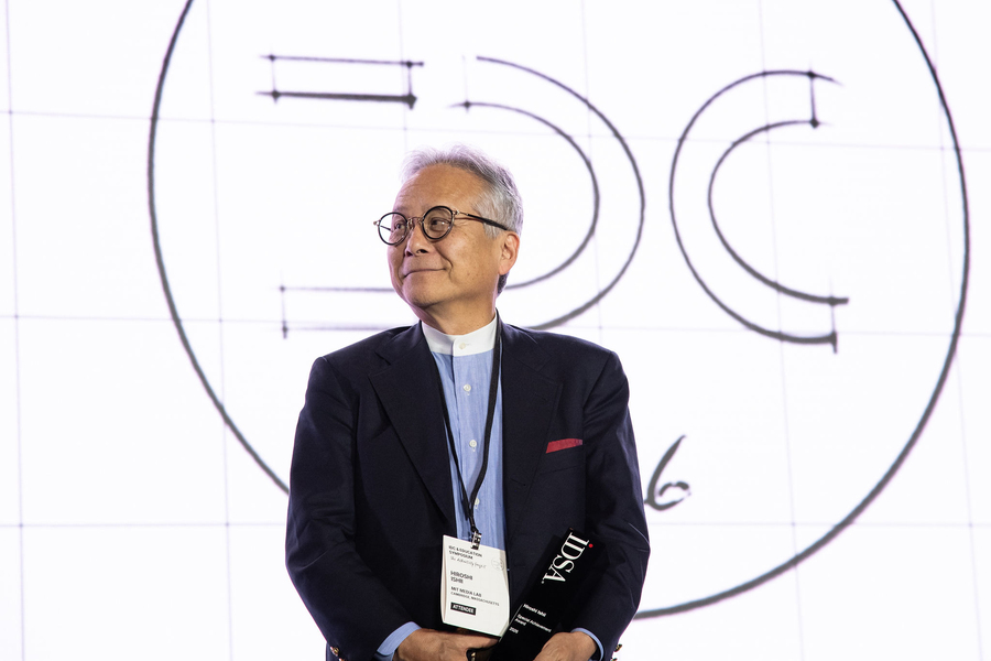 Hiroshi Ishii smiles on stage holding his black trophy.