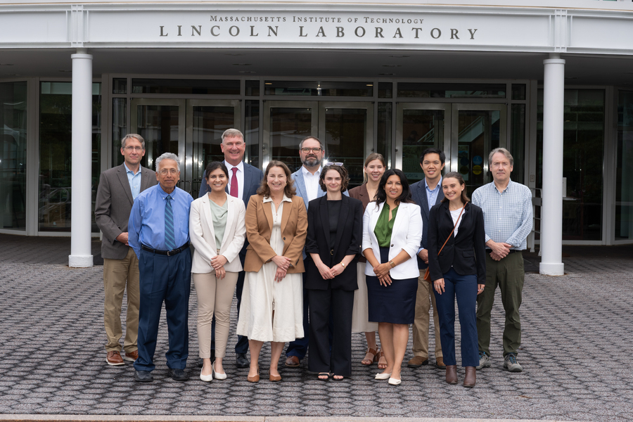 12 individuals pose for a group photo outside of Lincoln Laboratory