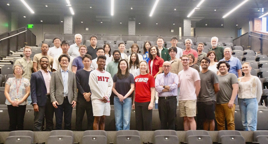 36 people stand together in rows of an auditorium and pose for a picture