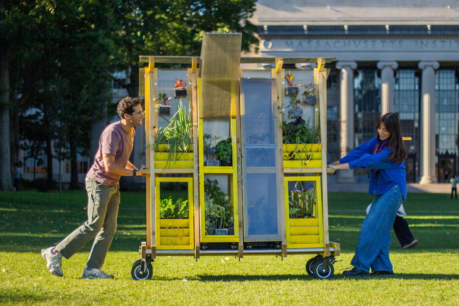 Zachary Rapaport pushes while Aleks Banaś pulls a tall cart holding plants in front of the MIT Dome