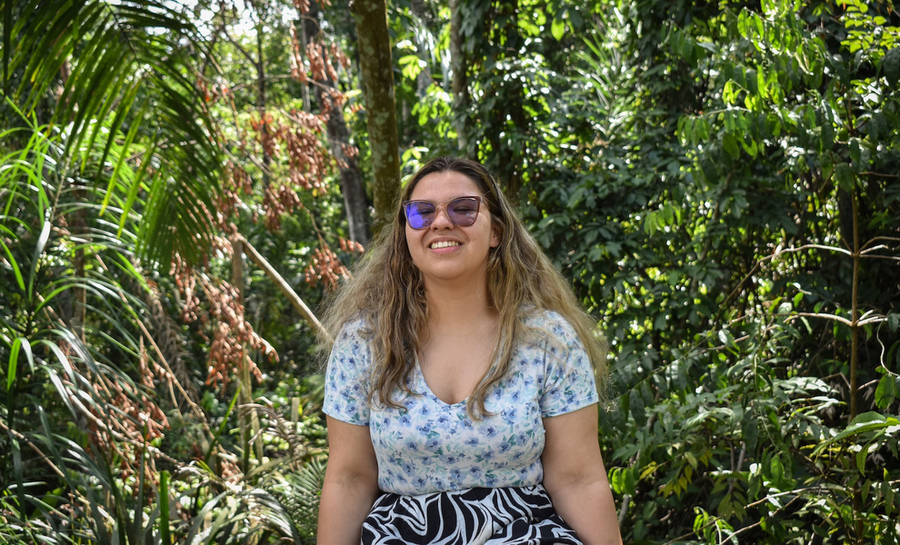 Hana Sousa sits in front of green trees in a rainforest on a sunny day 