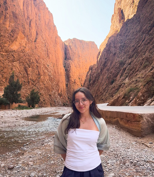 Isabel Duran stands in a sunlit canyon, on the margins of a riverbed
