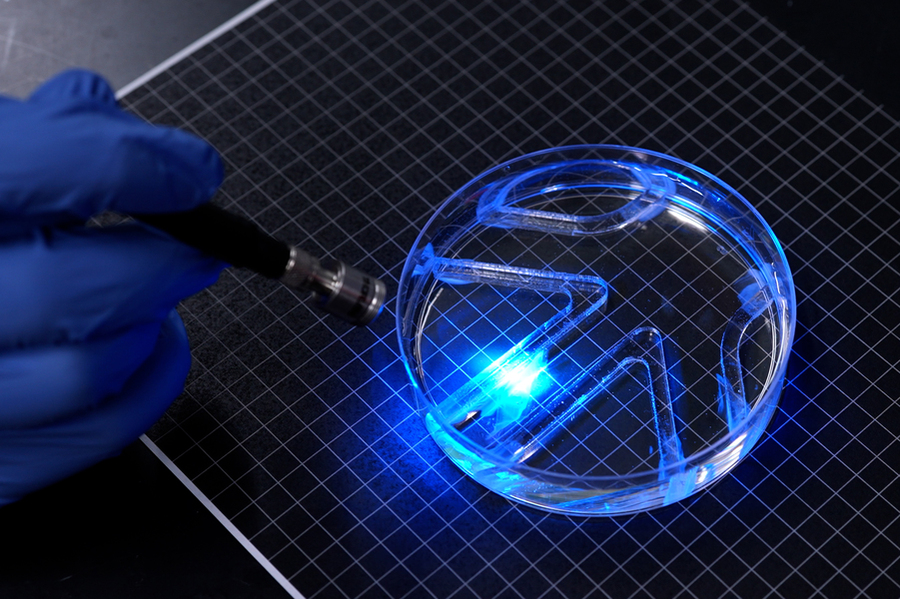 A bright blue light shines on a soft robot in a petri dish.