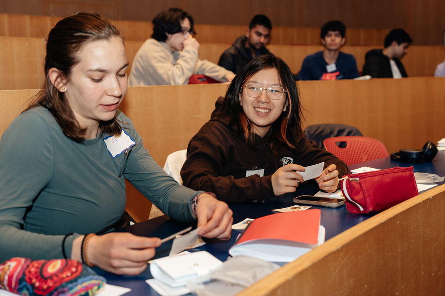 Student Sarah Hopp reviews her collection of intention cards in the foreground while a woman to her left smiles broadly. Other students are doing the same in the background.
