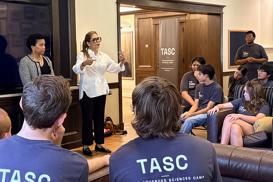 Nine students wearing TASC T-shirts listen to two women giving a presentation.