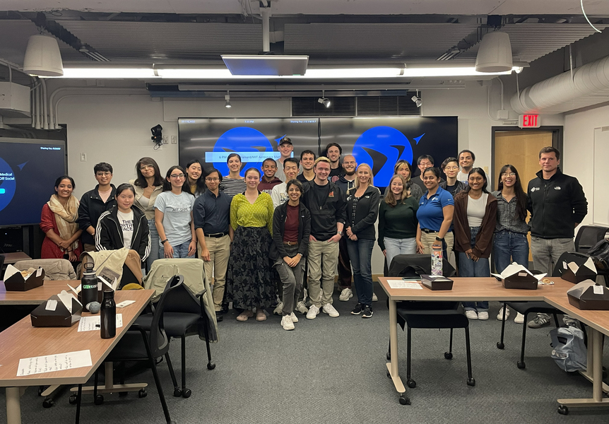 27 students and panelists pose standing in the front of a classroom