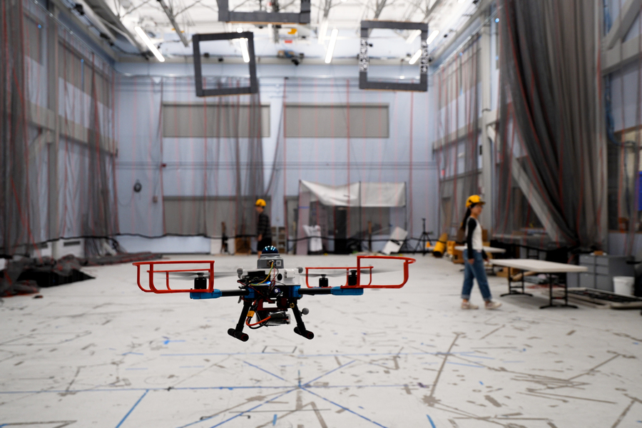 An autonomous drone flying in a space with two people in the background