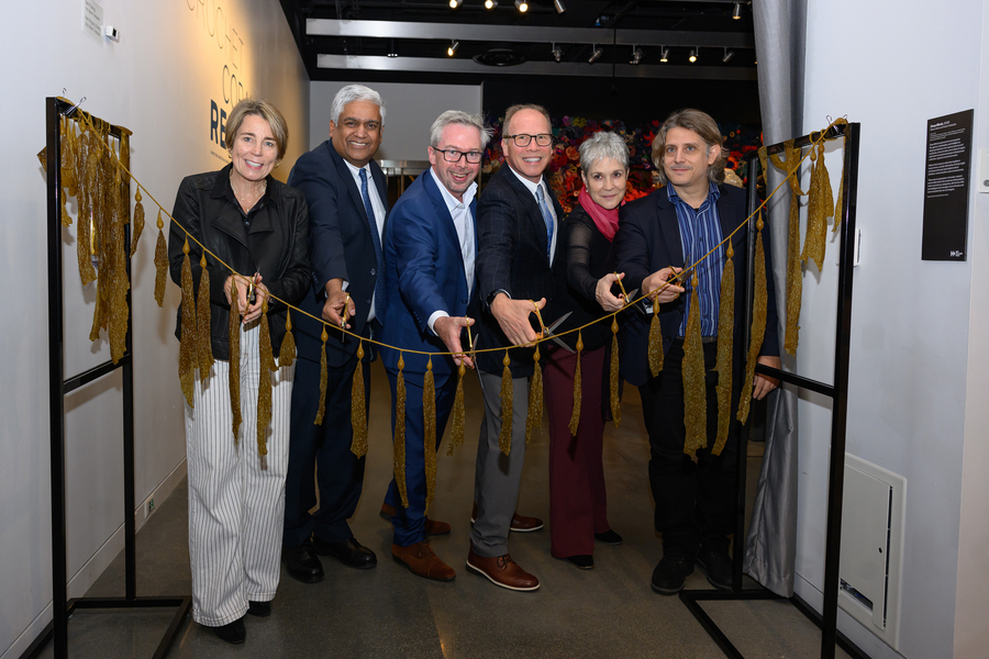 Six people hold out scissors to cut a long rope of kelp