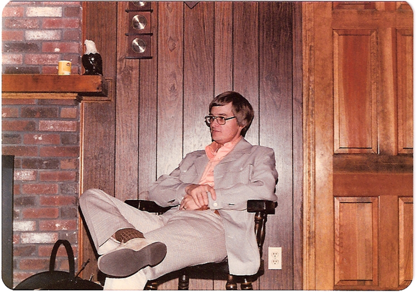 Gunter Stein as a young man, sitting next to a fireplace in a wood-paneled living room.