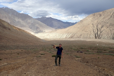 Photo of a man holding a pixaxe in the valley of a mountain range