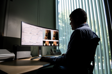 A researcher sits in an office looking at a computer monitor. On the left side of the monitor are several graphs. On the right side are four images of a woman's arm with a crown tattoo.