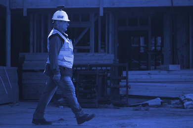 Blue-tinted photo of a construction worker walking on site with capture device on helmet