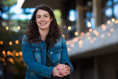 Portrait photo of Rachel Bielajew wearing a denim jacket, smiling, with her hands folded over her knee
